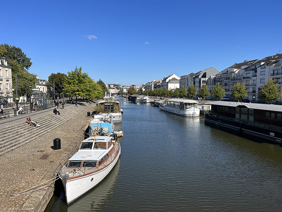 L'Erdre à Nantes vue depuis un pont : la rivière large et calme entre deux quais, des péniches et un yacht en bois amarrés le long des marches de pierre, immeubles clairs sur la rive droite