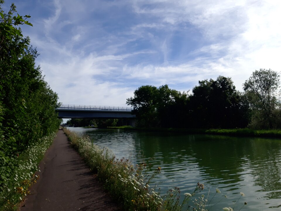 Le canal de la Marne au Rhin près de Strasbourg : eau verte et calme, chemin de halage sur la berge et pont routier au loin
