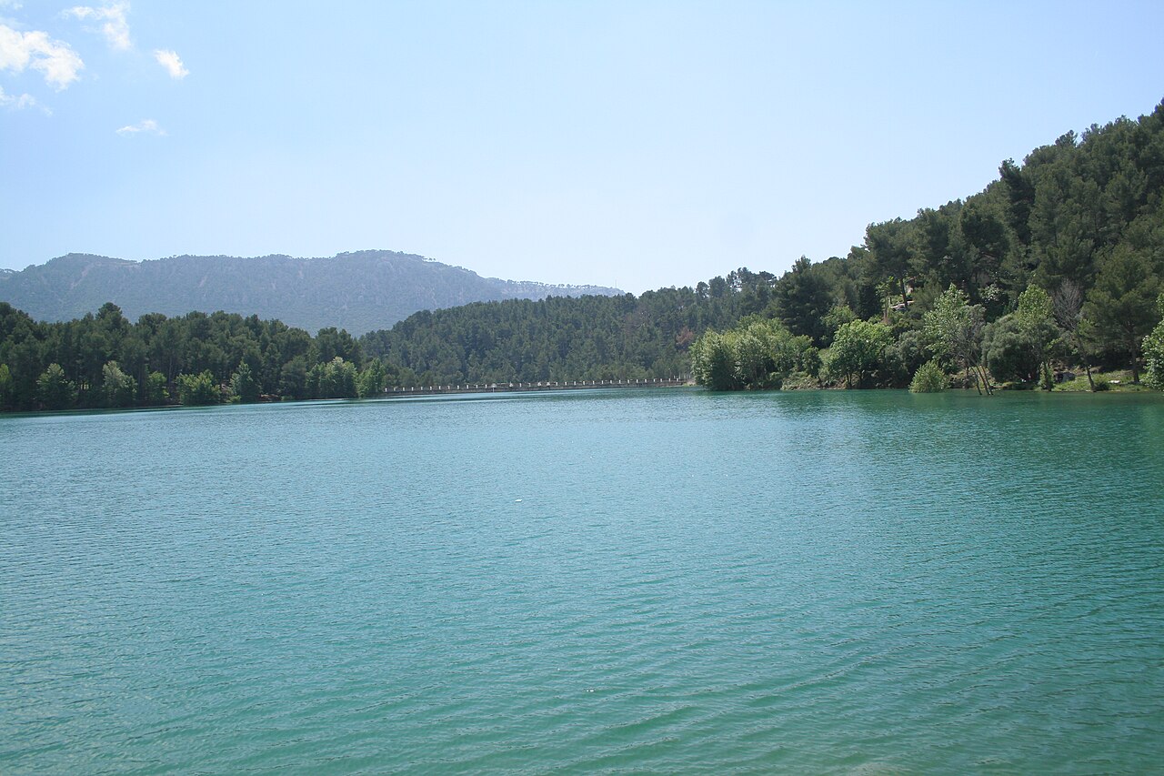 Le lac du Revest derrière le barrage de Dardennes : eau turquoise entourée de collines couvertes de pins, crête calcaire à l'horizon, mur du barrage visible au fond