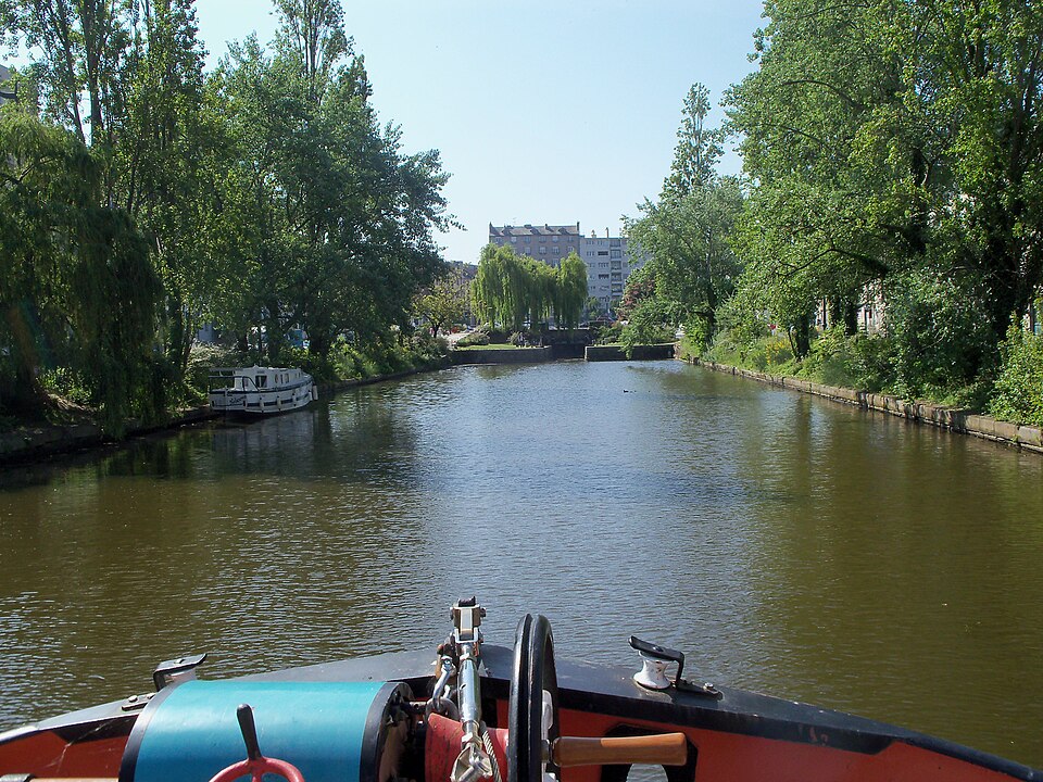 Le canal d'Ille-et-Rance à Rennes vu depuis l'avant d'un bateau : le bief bordé de saules et de peupliers, quelques bateaux amarrés à gauche, l'écluse du Mail fermant la perspective