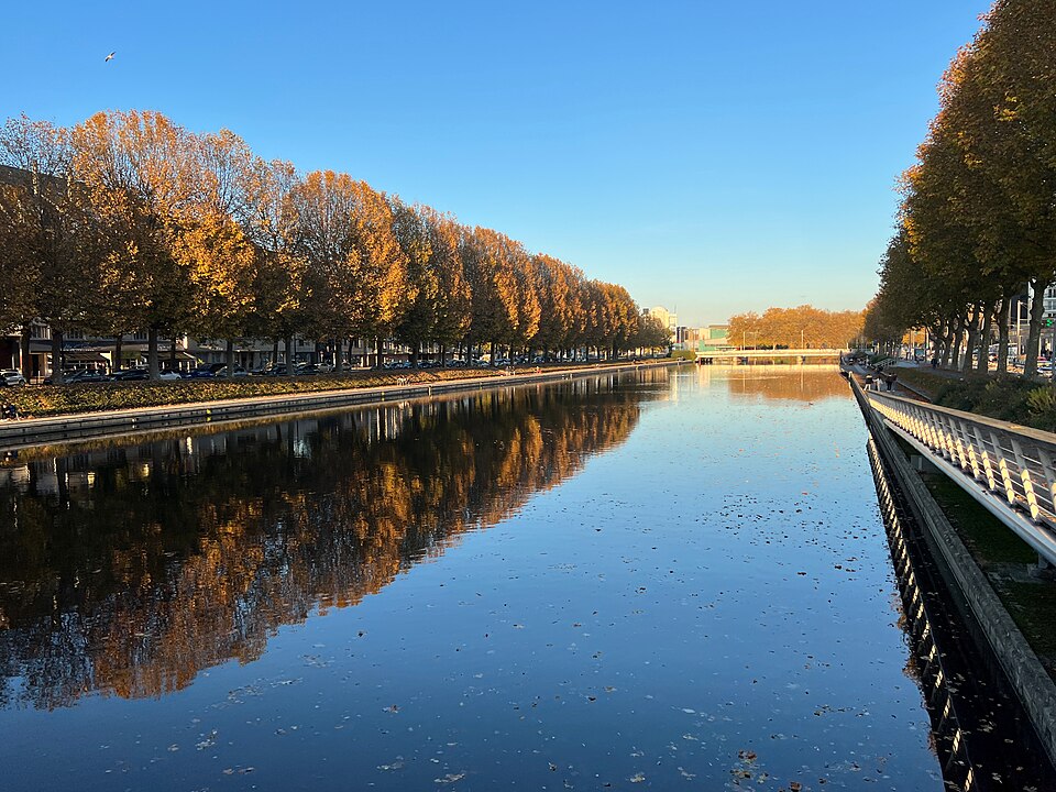 L'Orne à Caen vue depuis le pont Churchill en automne : la rivière canalisée entre deux quais, double rangée de platanes aux feuilles rousses se reflétant dans l'eau calme, garde-corps blanc sur la rive droite