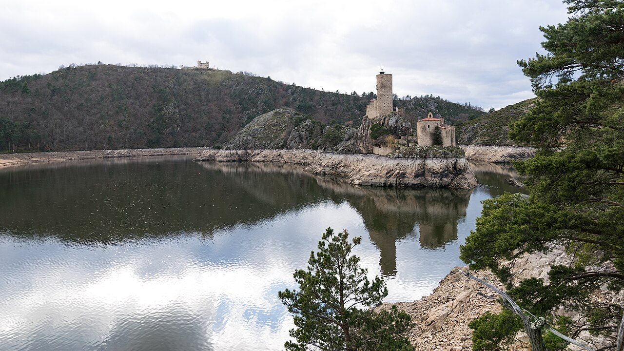 Le lac de Grangent dans les gorges de la Loire : eau calme entre des versants boisés, le château de Grangent sur son îlot rocheux, ligne de marnage claire sur les rives