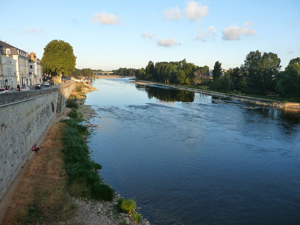 La Loire à Orléans en eau basse vue depuis un pont : le fleuve large et peu profond, bancs de graviers et îles boisées au milieu du lit, mur de quai en pierre et berge caillouteuse à gauche