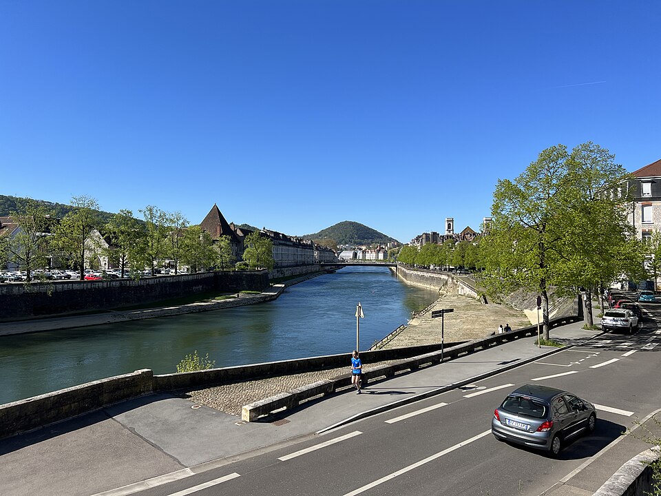 Le Doubs à Besançon vu depuis un pont : la rivière large et verte entre deux quais de pierre, immeubles anciens sur la rive gauche, colline boisée au fond
