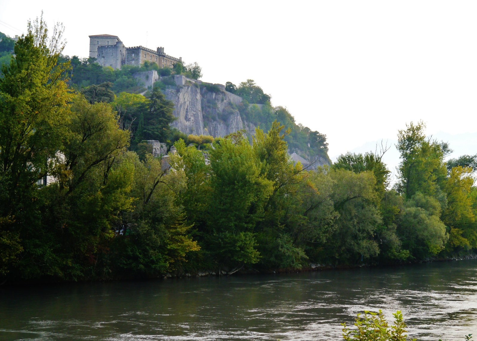 L'Isère à Grenoble : une rivière large et rapide aux eaux vert-gris, bordée d'arbres, avec la falaise de la Bastille et son fort en surplomb